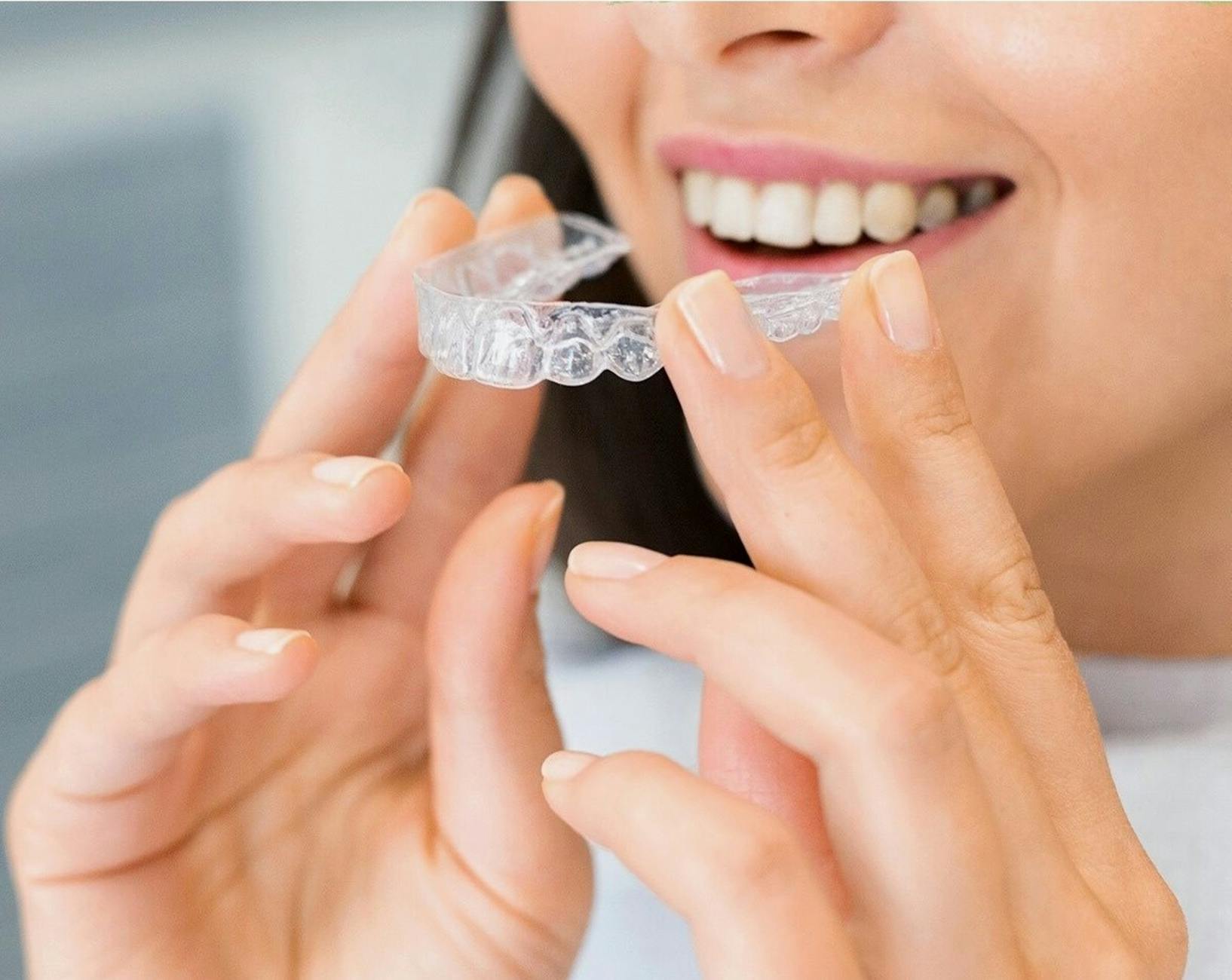 Uśmiechnięta kobieta trzyma przezroczystą nakładkę Invisalign przy zębach