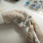 Dentysta w rękawiczkach obrabia precyzyjnie małą protezę zębową
