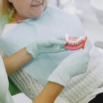 Dentystka pokazuje starszej kobiecie prawidłowe czyszczenie protezy