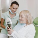 Starsza kobieta z dentystą ogląda protezę zębową w lusterku
