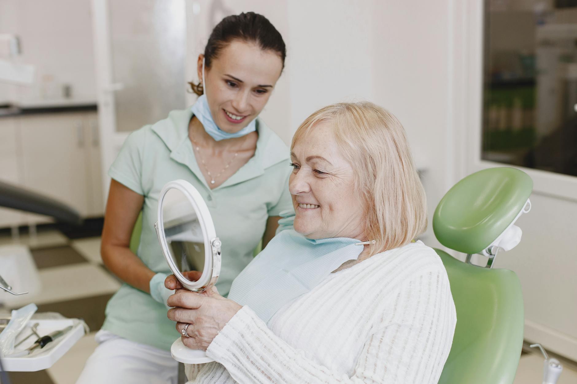 Starsza kobieta z dentystą ogląda protezę zębową w lusterku