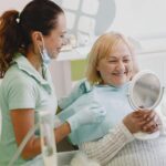 Starsza pacjentka u dentysty, uśmiecha się podczas przeglądu zębów