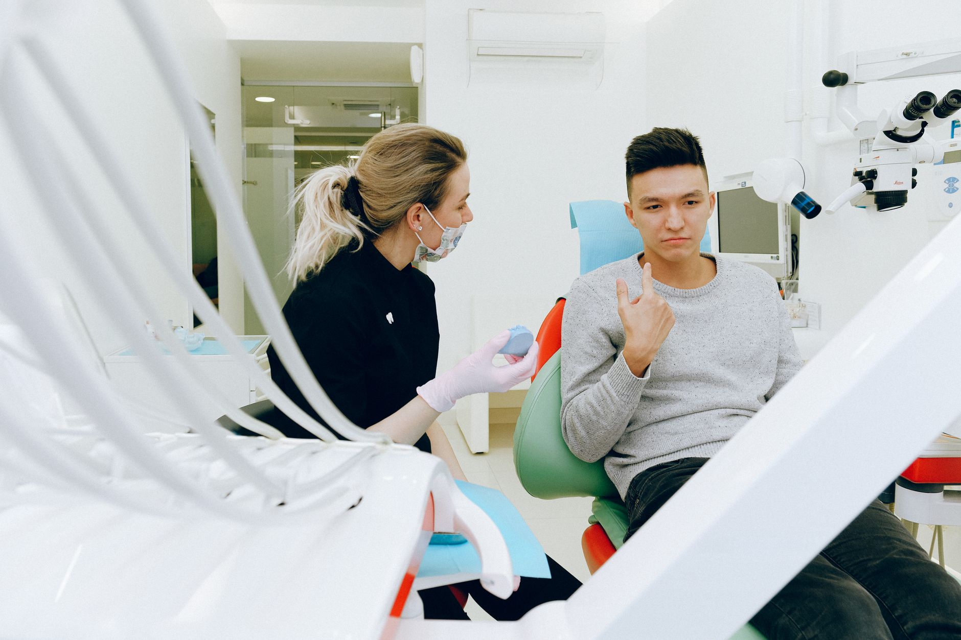 Dentysta w rękawiczkach pokazuje pacjentowi model zęba po endodoncji