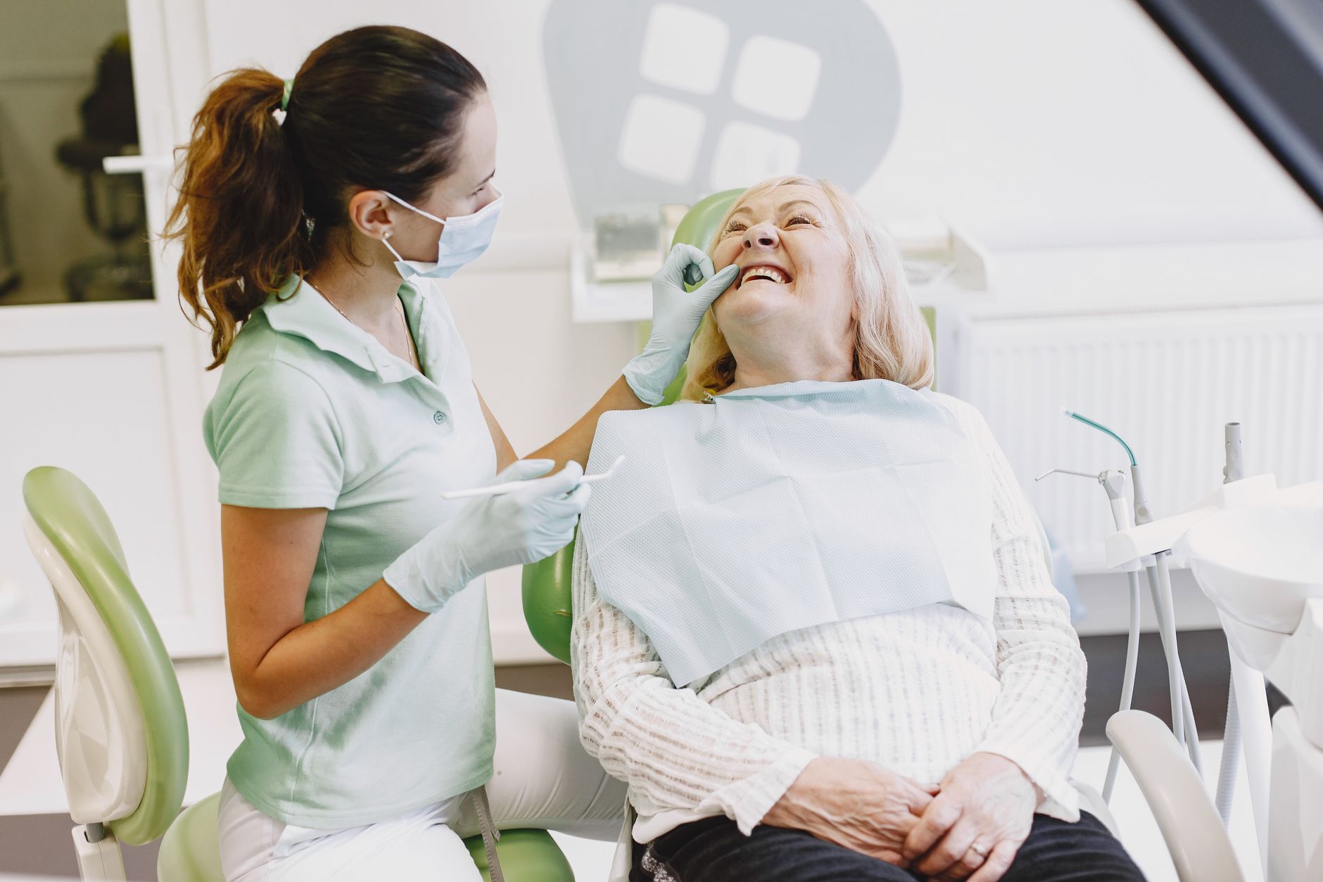 Dentystka bada uśmiechniętą starszą pacjentkę w gabinecie