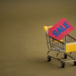 Mały wózek sklepowy z czerwoną etykietą SALE na brązowym tle